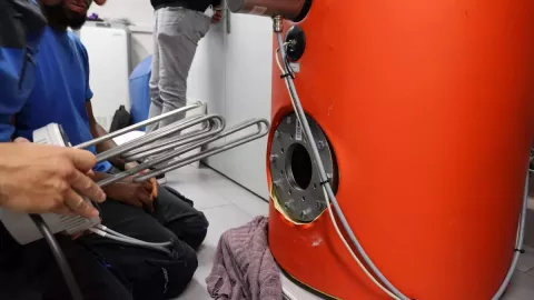 Ein Installateur baut den Heizstab in einen Wassertank ein.
